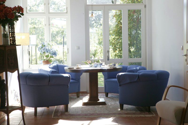Blaue Sessel um einen runden Tisch vor großen Fenstern